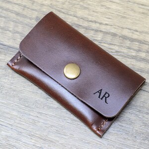 May include: A brown leather key holder with a brass button closure and the initials "AR" embossed on the front.