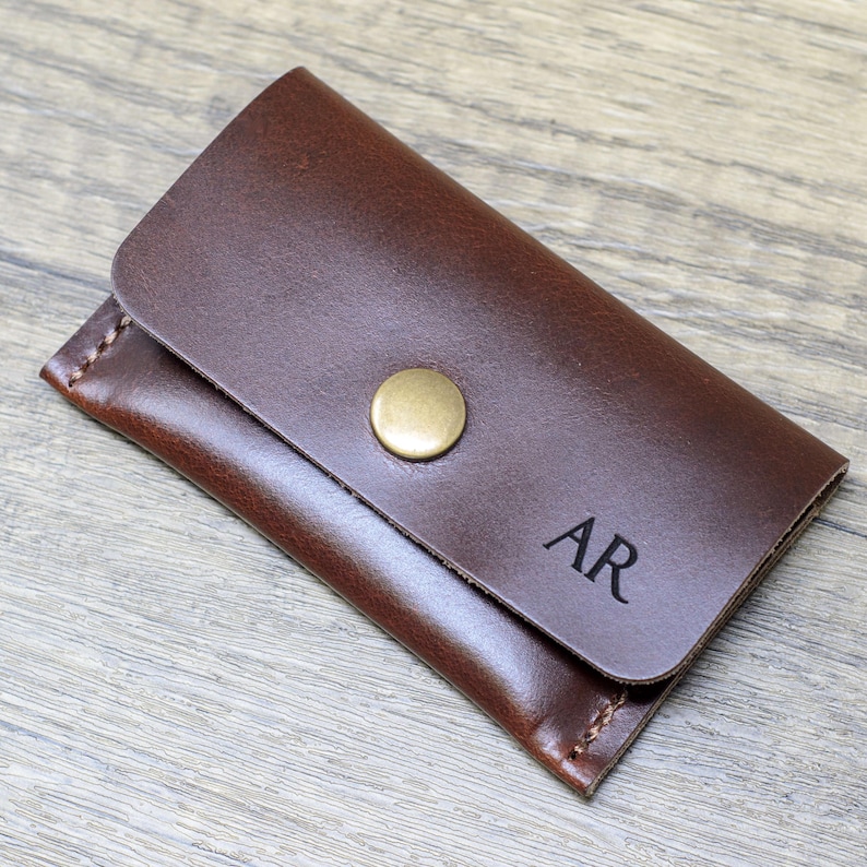 May include: A brown leather key holder with a brass button closure and the initials "AR" embossed on the front.