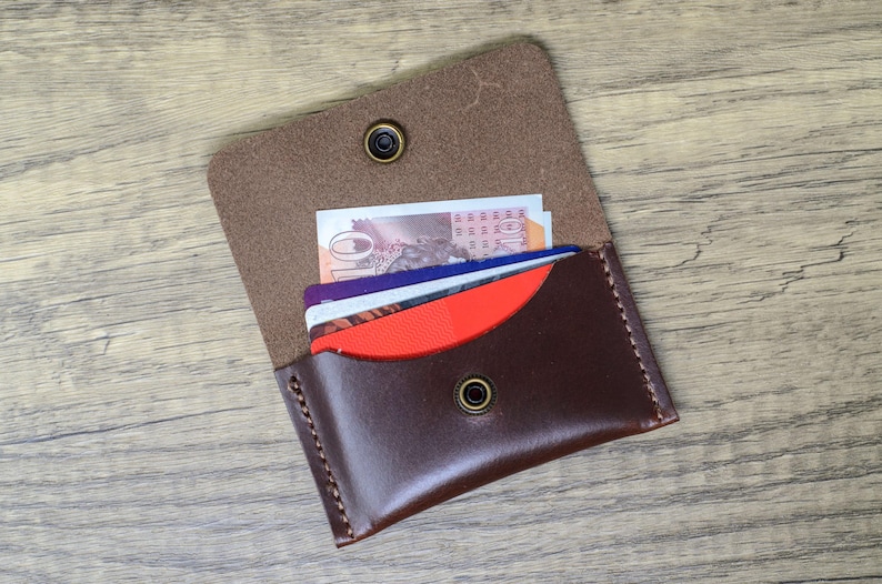 May include: A brown leather wallet with a flap that opens to reveal a red and blue card holder. The wallet has two brass snaps and is filled with credit cards and cash.