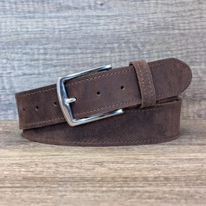 May include: A brown leather belt with a silver buckle. The belt is folded in half and the buckle is in the centre of the image.