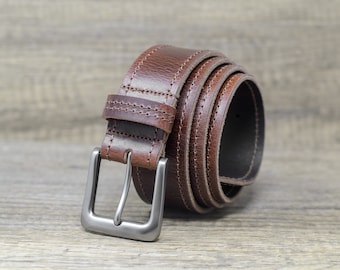 May include: A brown leather belt with a silver buckle. The belt is rolled up and the buckle is facing the camera.