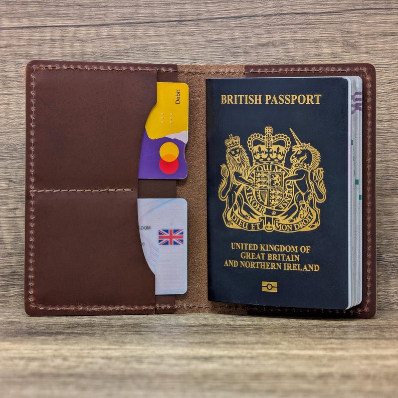May include: A brown leather passport holder with a British passport inside. The passport holder has slots for cards and a pocket for cash. The passport holder is open and the passport is visible.