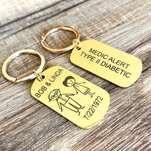May include: Two gold-toned keychains with engraved text. One keychain has the text "Medic Alert Type II Diabetic" and the other keychain has the text "Bob & Linda 7/22/1972" with a stick figure drawing of a couple.