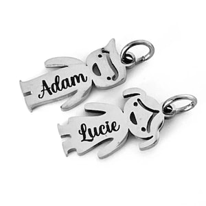 K&ouml;nnte beinhalten: Zwei silberne Anh&auml;nger in Form von Strichm&auml;nnchen, ein Junge und ein M&auml;dchen. Der Jungenanh&auml;nger hat den Namen "Adam" eingraviert und der M&auml;dchenanh&auml;nger den Namen "Lucie".