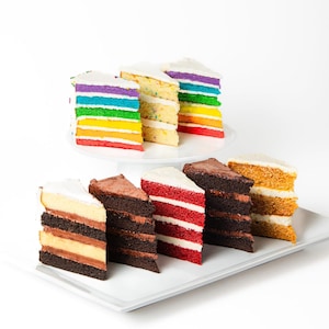 May include: Assortment of layered cakes with different flavors and colors. The cakes are arranged on two white cake stands. The cakes include rainbow, red velvet, chocolate, and vanilla.