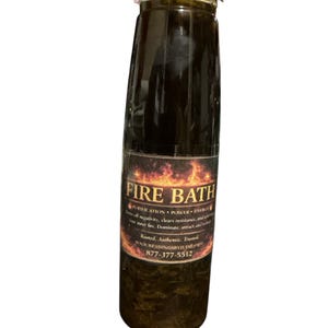 Puede incluir: Una botella transparente con tapa blanca, llena de líquido oscuro. La etiqueta dice "FIRE BATH" con texto sobre purificación y poder. El líquido oscuro contiene partículas visibles.