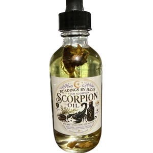 Può includere: Una bottiglia di vetro trasparente con un contagocce nero riempita di olio giallo. L'etichetta recita "Readings by Judie Team Scorpion Oil" con un'illustrazione di scorpione. La bottiglia contiene materiale vegetale.