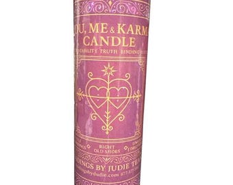 May include: A tall, cylindrical candle with a pink label featuring gold decorative elements and the text "OU, ME & KARM CANDLE". The label also includes the words "STABILITY TRUTH BINDING" and "RIGHT OLD SHOES".