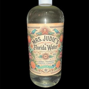 Peut inclure: Une bouteille en verre transparent contenant un liquide avec une étiquette indiquant Mrs. Judie's Florida Water, A Herbal Fragrance & Spiritual Cleaning. L'étiquette présente des illustrations d'oranges, d'oiseaux, d'un soleil et d'un œil, avec 33 et 1933.