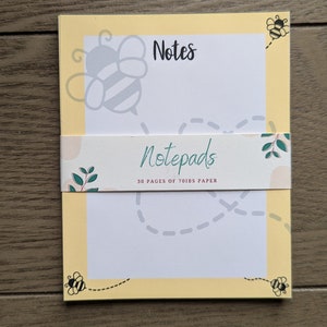 Puede incluir: Un bloc de notas amarillo con un diseño de abeja y el texto "Notes" y "Notepads 30 pages of 70lbs paper".