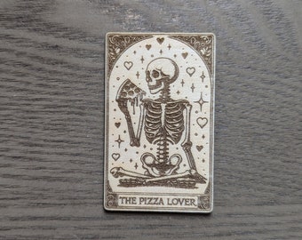 May include: A wooden card with a skeleton eating a slice of pizza. The card is decorated with hearts and stars. The text "THE PIZZA LOVER" is printed at the bottom of the card.