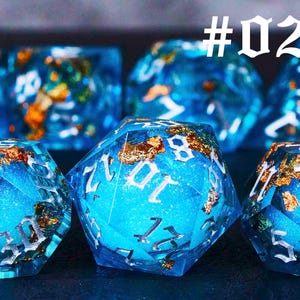 Puede incluir: Un conjunto de dados azules y dorados con n&uacute;meros blancos. Los dados est&aacute;n hechos de resina y tienen un acabado brillante. #02