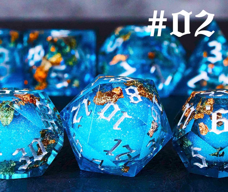 Puede incluir: Un conjunto de dados azules y dorados con n&uacute;meros blancos. Los dados est&aacute;n hechos de resina y tienen un acabado brillante. #02