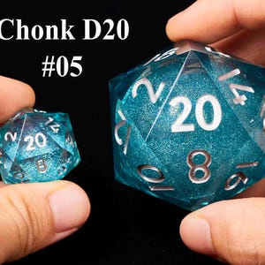May include: Two turquoise blue D20 dice with silver numbers. The larger die has a glittery finish and the smaller die has a smooth finish. The larger die has the text "Chonk D20 #05" above it.