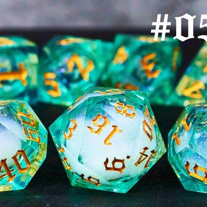 Puede incluir: Un conjunto de diez dados de color verde azulado con n&uacute;meros dorados y un interior blanco nublado. Los dados est&aacute;n numerados del 1 al 6. Los dados est&aacute;n dispuestos en c&iacute;rculo con el n&uacute;mero 5 hacia arriba. #05