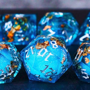 May include: A set of blue and gold dice with white numbers. The dice are made of resin and have a sparkly finish.