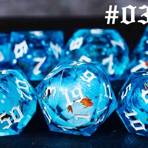 Puede incluir: Un conjunto de dados azules con n&uacute;meros blancos y un dise&ntilde;o de pez. Los dados est&aacute;n hechos de pl&aacute;stico transparente y tienen un acabado brillante. Los dados est&aacute;n numerados del 1 al 6. #03