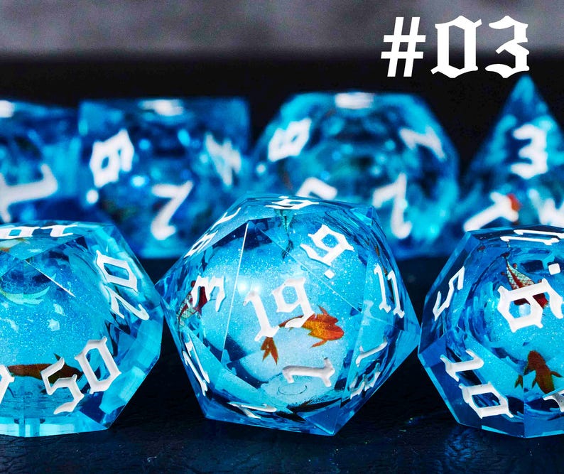 Puede incluir: Un conjunto de dados azules con n&uacute;meros blancos y un dise&ntilde;o de pez. Los dados est&aacute;n hechos de pl&aacute;stico transparente y tienen un acabado brillante. Los dados est&aacute;n numerados del 1 al 6. #03
