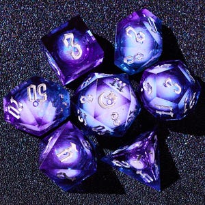 Puede incluir: Conjunto de siete dados iridiscentes de color morado y azul con números y símbolos blancos. Los dados están hechos de un material transparente con un efecto de remolino.
