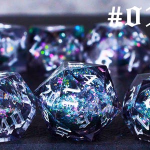 Puede incluir: Un conjunto de dados iridiscentes con n&uacute;meros negros, que presentan un dise&ntilde;o brillante tipo galaxia. Los dados est&aacute;n hechos de resina transparente y tienen una variedad de colores, incluyendo azul, morado y verde.