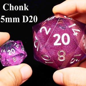 May include: Two purple D20 dice with white numbers and glitter. The larger die is 55mm and the smaller die is 20mm.