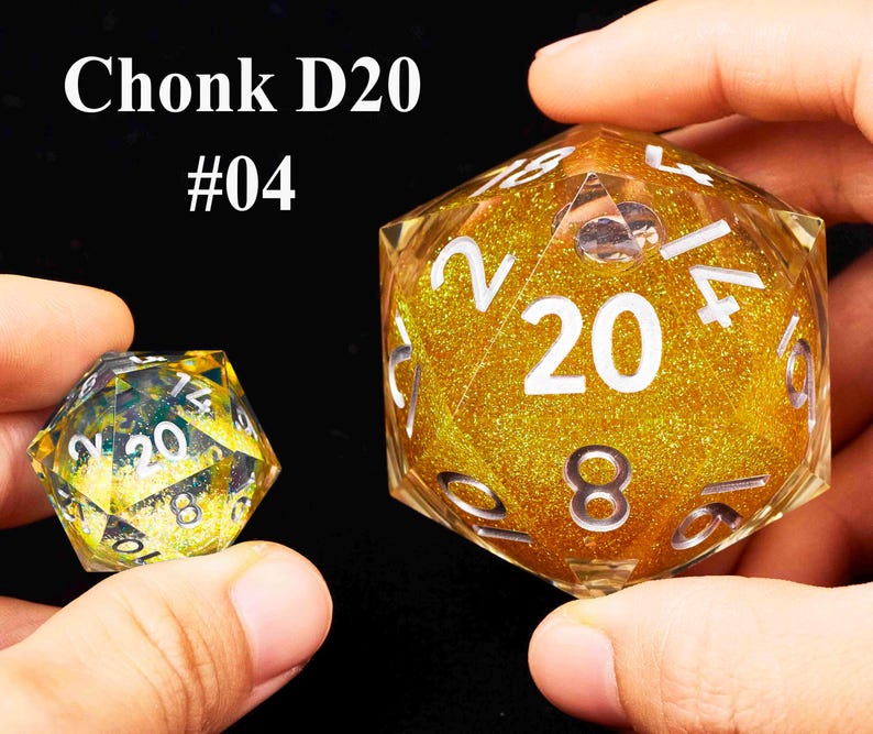 May include: Two gold glitter filled twenty-sided dice, one large and one small. The larger die has the number 20 printed on it in white. The smaller die has the number 20 printed on it in white. The dice are labeled "Chonk D20 #04".