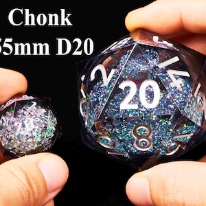 May include: A large, 55mm iridescent blue and purple D20 dice with white numbers and glitter. The dice is being held in a hand.