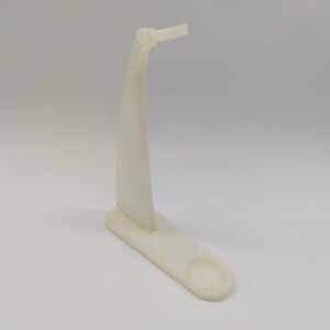 May include: White plastic stand with a curved arm and a round base. The stand is designed to hold a small object, such as a phone or a pen.