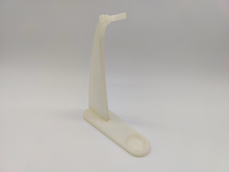 May include: White plastic stand with a curved arm and a round base. The stand is designed to hold a small object, such as a phone or a pen.