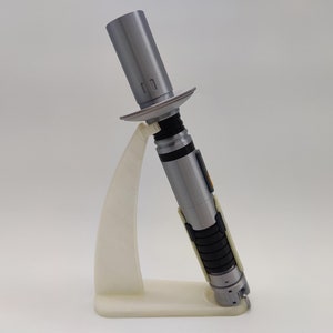 May include: A silver lightsaber with black and white accents is displayed on a white plastic stand. The lightsaber is in a deactivated state.
