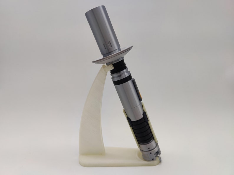 May include: A silver lightsaber with black and white accents is displayed on a white plastic stand. The lightsaber is in a deactivated state.
