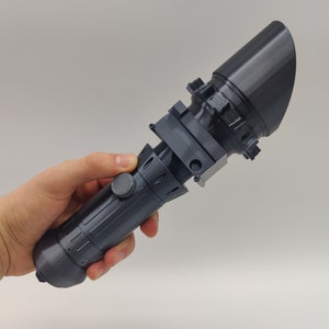 May include: A black plastic prop weapon with a cylindrical handle and a flared end. The handle has a textured surface and a small knob on the side.