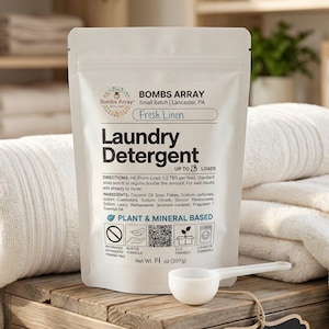 May include: A white pouch of "Fresh Linen" laundry detergent with a measuring scoop. The package reads "Laundry Detergent" and "Plant & Mineral Based." The net weight is 14 oz (397g). The background includes white towels and a wooden surface.