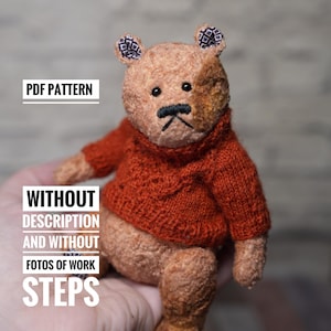May include: A small, brown teddy bear wearing a red knitted sweater. The bear has a brown patch on its face and black eyes. The bear is sitting in a hand.