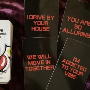 Puede incluir: Una baraja de cartas de tarot Love Message con un diseño blanco y rojo. La baraja incluye cartas con frases como "I drive by your house" y "You are so alluring."