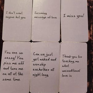May include: Six rectangular cards with handwritten text. The cards have phrases like "I don't want anyone but you," "Incoming message of love," and "I miss you!" The cards are arranged on a dark, textured surface.