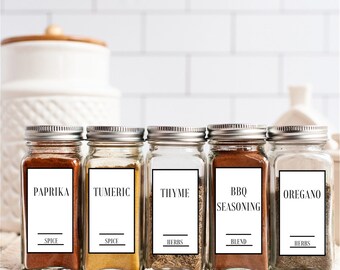 May include: Five glass spice jars with black labels and white text. The labels read "Paprika Spice", "Turmeric Spice", "Thyme Herbs", "BBQ Seasoning Blend", and "Oregano Herbs".