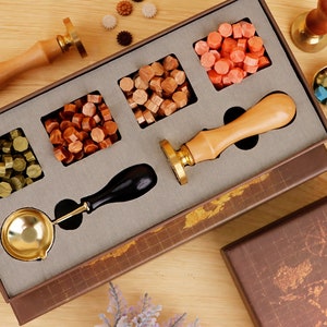 May include: A wooden box with a variety of wax seal supplies, including a wax melting spoon, a wooden handle wax stamp, and four different colors of wax pellets. The box has a world map design on the inside.