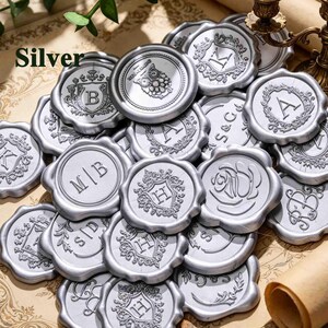 May include: A collection of silver wax seals featuring various embossed designs including letters, monograms, a rose, and an owl. The word Silver is printed in the upper left corner. Each circular seal has a scalloped edge and a metallic finish.