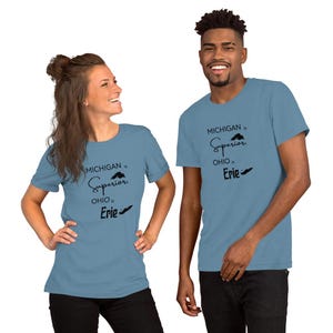 Peut inclure: Deux personnes portent des t-shirts bleu clair. Les t-shirts affichent le texte "MICHIGAN is Superior, OHIO is Erie" en noir. Les t-shirts sont à manches courtes et faits d'une matière douce.