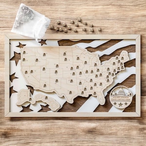 May include: A wooden map of the United States with a white and brown striped background. The map is in a frame and has a circle in the bottom right corner that says "HOLMES ANDRUS STATE CAPITALS MAP".