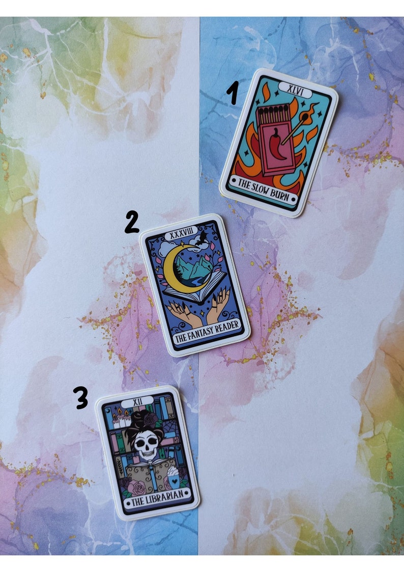 K&ouml;nnte beinhalten: Drei Tarotkarten-Aufkleber mit bunten Illustrationen und Text. Der erste Aufkleber ist blau mit einer roten Chilischote und Streichh&ouml;lzern und dem Text "XLVI THE SLOW BURN". Der zweite Aufkleber ist lila mit einem Halbmond, Bergen und H&auml;nden, die ein Buch halten, und dem Text "XXXVII THE FANTASY READER". Der dritte Aufkleber ist lila mit einem Sch&auml;del, der eine Krone tr&auml;gt und ein Buch h&auml;lt, und dem Text "XII THE LIBRARIAN".