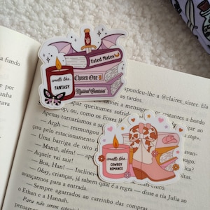 May include: Three pink and purple sticker designs featuring stacks of books with a candle on top. The candles are labeled "smells like... FANTASY" and "smells like... COWBOY ROMANCE". The books are labeled "Fated Mates", "Chosen One", and "Mystical Creatures".