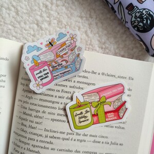 May include: Three pink and green book-themed stickers with illustrations of candles and books. The text on the stickers reads "Smells Like Small Town Romance", "Smells Like Holiday Romance", "Met Cute", "County Fair", "Nosey Neighbours", "Christmas Tree Farm", and "Small Town Romance".