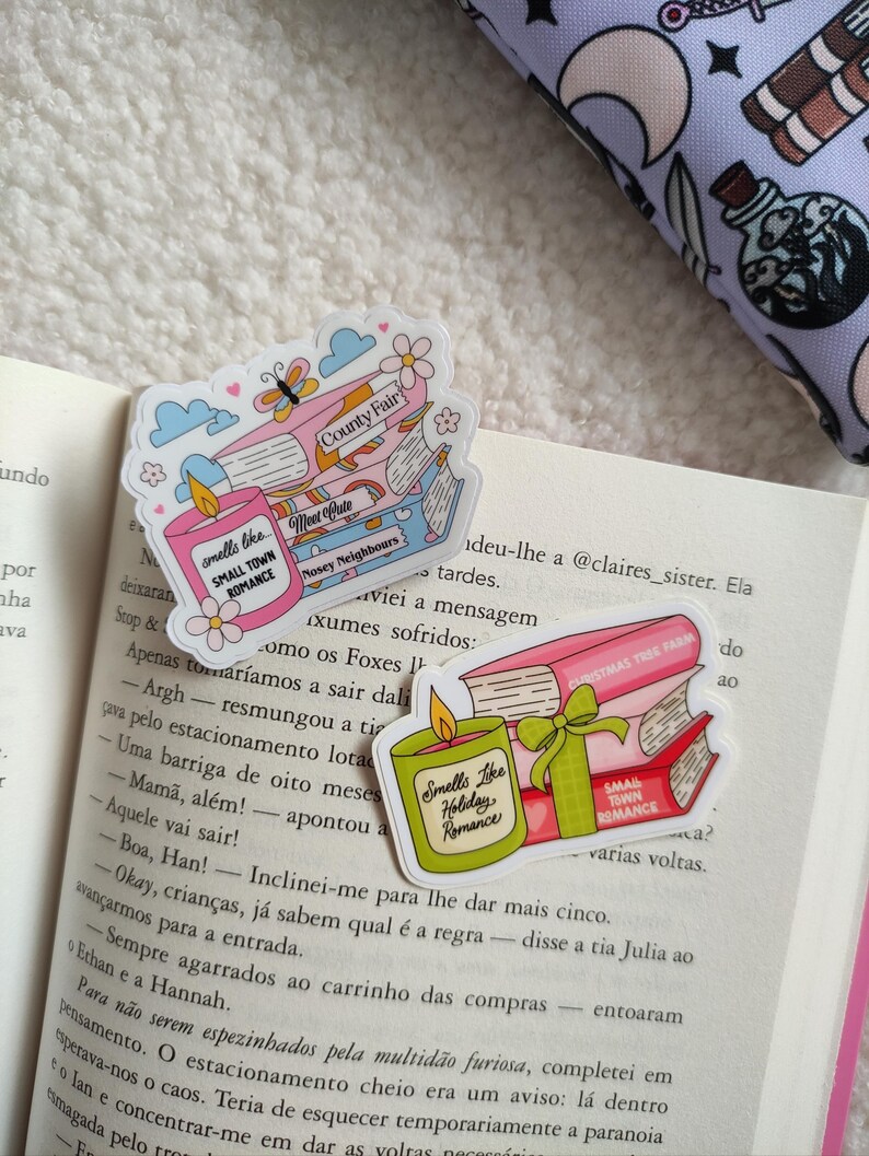 May include: Three pink and green book-themed stickers with illustrations of candles and books. The text on the stickers reads "Smells Like Small Town Romance", "Smells Like Holiday Romance", "Met Cute", "County Fair", "Nosey Neighbours", "Christmas Tree Farm", and "Small Town Romance".
