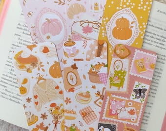 May include: A collection of decorative bookmarks with autumn-themed illustrations. The bookmarks feature pumpkins, fall leaves, cozy sweaters, and teacups in shades of orange, pink, and yellow. They are designed for book lovers.