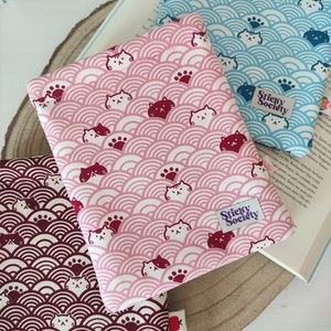 Pode incluir: Três capas de livros em rosa, azul e bordô com um padrão repetitivo de gatos brancos e pegadas em um design de ondas. Cada capa tem um pequeno rótulo retangular com o texto "Sticky Society" em letras brancas sobre fundo roxo.