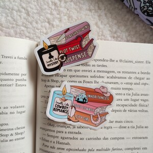 May include: Three colorful book stack stickers with a candle on top. The candle is labeled "Smells Like Cowboy Romance". The book stacks are labeled "Fore shadowing", "Plot Twist", "Suspense", "Inheritances", "Rodeo Cowboy", and "City Girl".