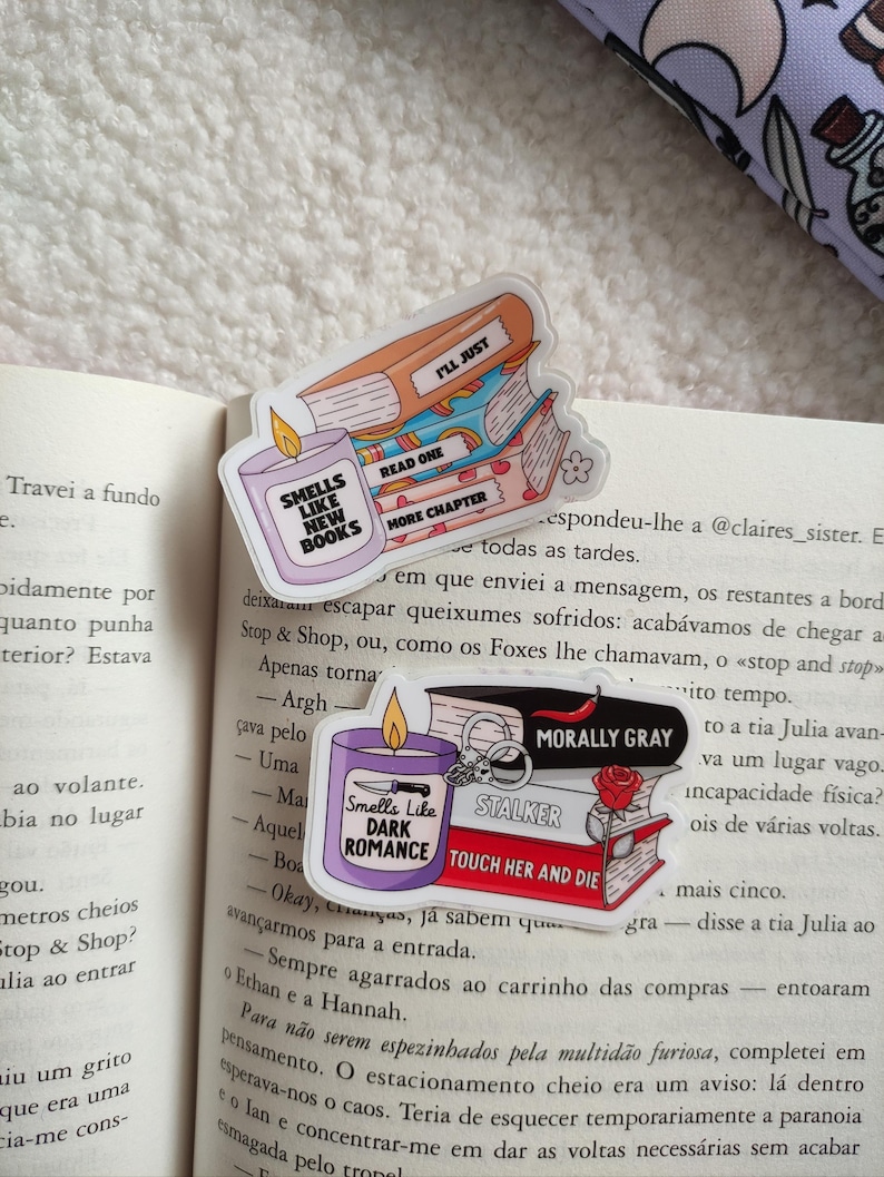 May include: Three colorful book-themed stickers with text that reads "Smells Like New Books", "Read One More Chapter", and "I'll Just". The stickers are layered on top of each other and feature a candle, a book, and a book with a bookmark. The stickers are on a white background.