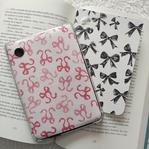 Peut inclure: Gros plan sur deux couvertures de livres avec un étui de téléphone à motifs roses et blancs sur le dessus. L'étui de téléphone présente un motif de nœuds roses sur fond blanc. Les couvertures de livres présentent un motif de nœuds noirs sur fond blanc. Le texte sur la couverture du livre est "dela. Tin untaram".